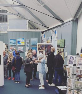 Busy hART 2023 exhibition with visitors and artwork inside the Tin Tabernacle in Hythe.