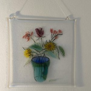 Floral fused glass artwork by Caroline Raffan showing colourful wildflowers arranged in a blue and green glass vase.