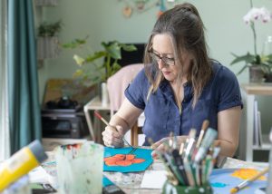 Artist Fiona Yorke-Saville painting colourful floral artwork in her studio.