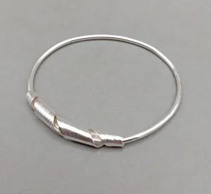 Contemporary silver bangle by Julian Warrender featuring a textured overlapping detail wrapped around the polished band.
