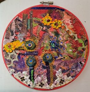 Circular textile artwork by Olga Van Dijke combining layered fabrics, fibres, embroidery and colourful floral details.