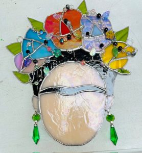 Stained glass portrait of Frida Kahlo by Yolanda Houston, featuring a colourful floral headdress, beaded details and green glass earrings.