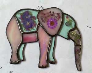 Stained glass elephant by Yolanda Houston in soft pink and turquoise glass, decorated with pressed flowers and botanical details.